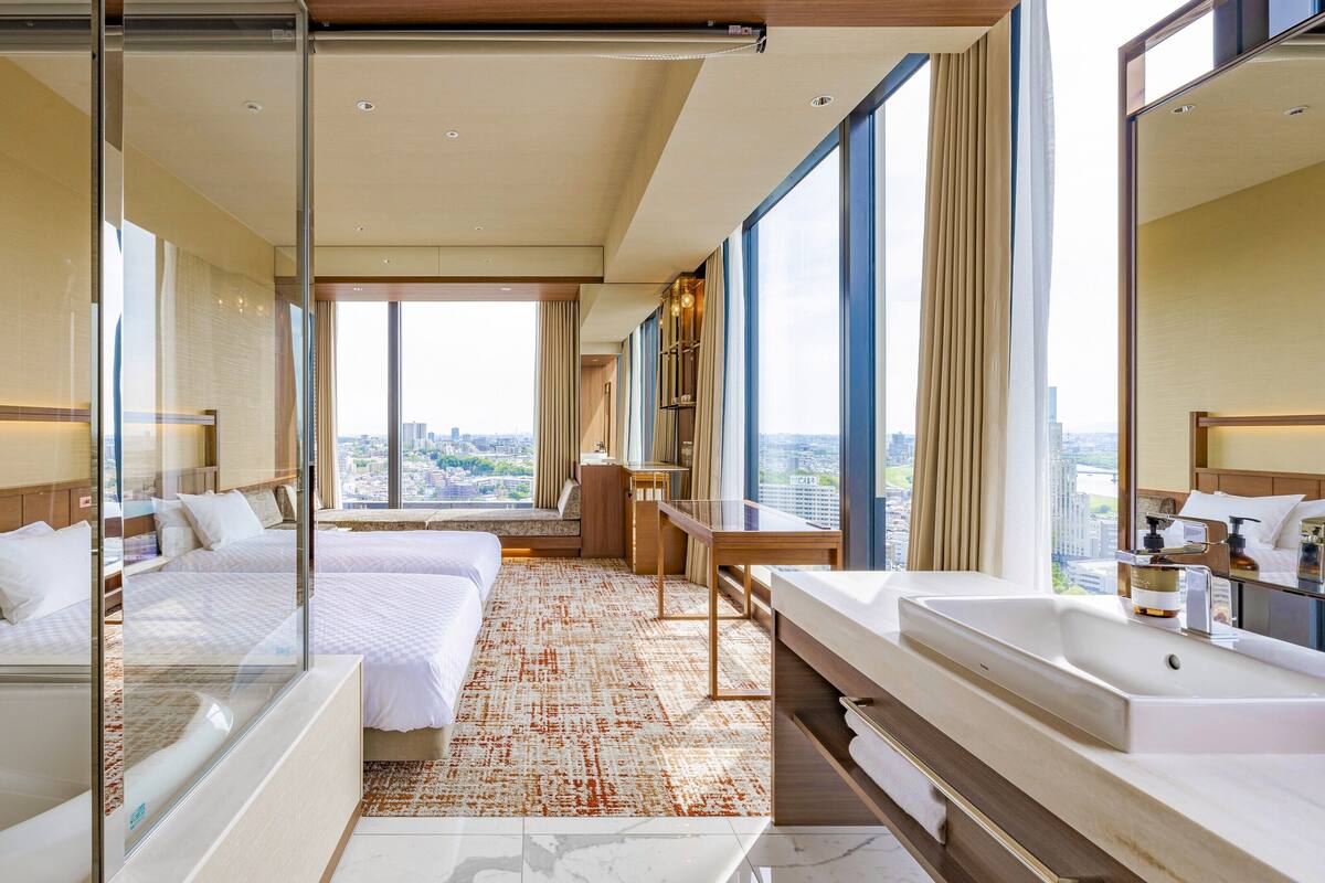 Hotelkamer met een groot bed, een kleiner bed, een badkamer met bad en uitzicht op de stad.