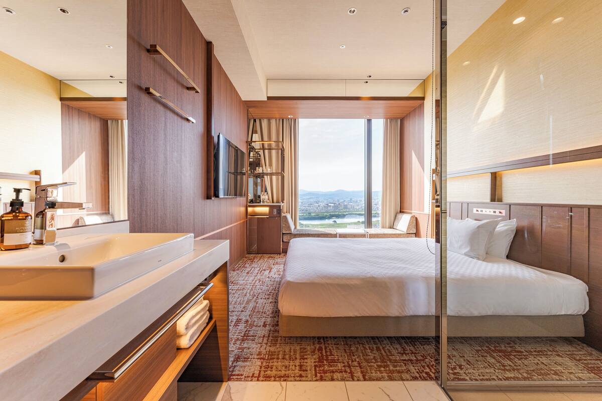 Een moderne hotelkamer met een groot bed, een badkamer met een wastafel en uitzicht op de stad.