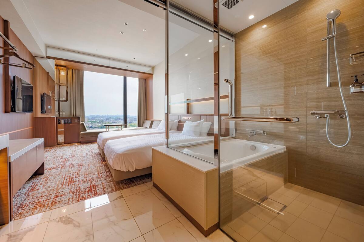 Een moderne hotelkamer met een groot bed, een aparte badkamer met badkuip en uitzicht op de stad.