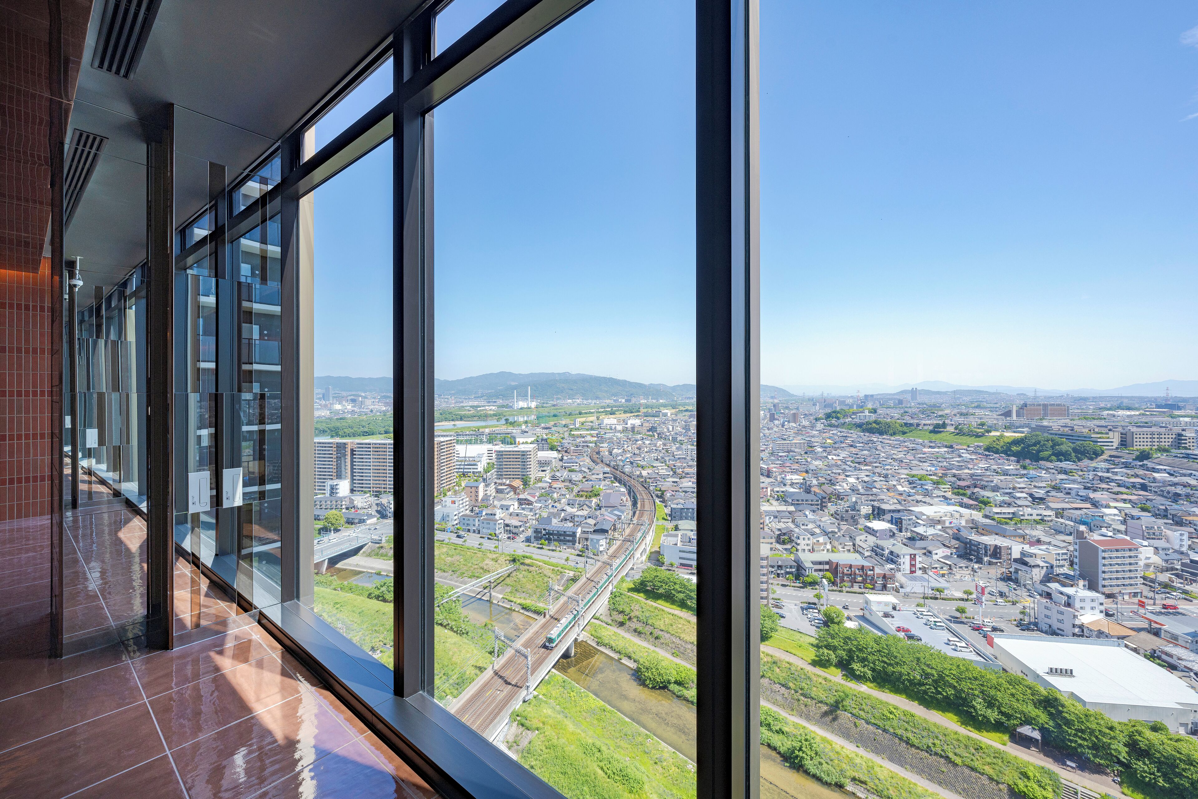 A high-rise building with large windows offering a view of a cityscape and a railway track.