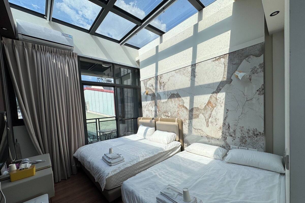 A hotel room with two beds, a large window, and a view of the outside.