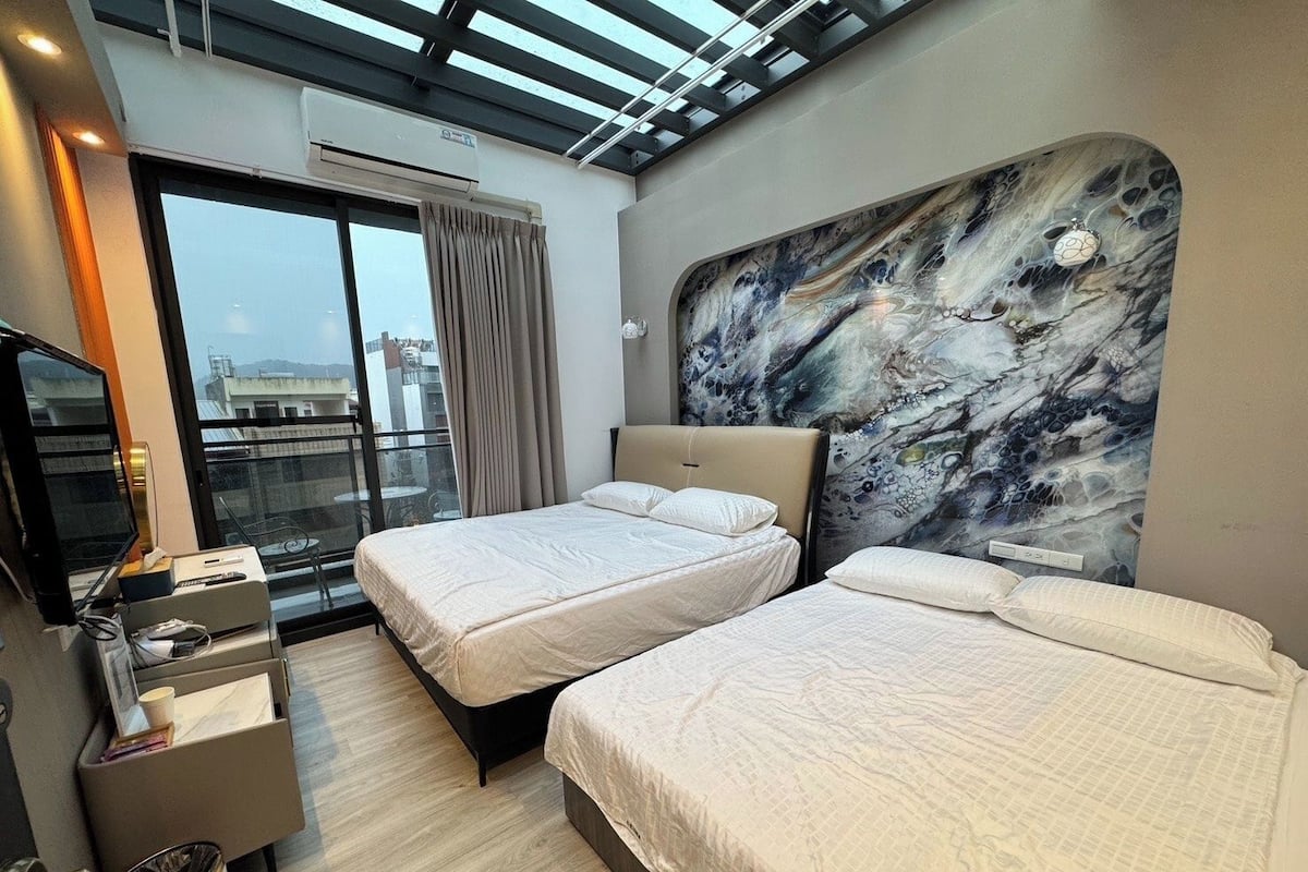 A modern hotel room with two beds, a large window with a view, a flat-screen TV, and a marble-patterned headboard.
