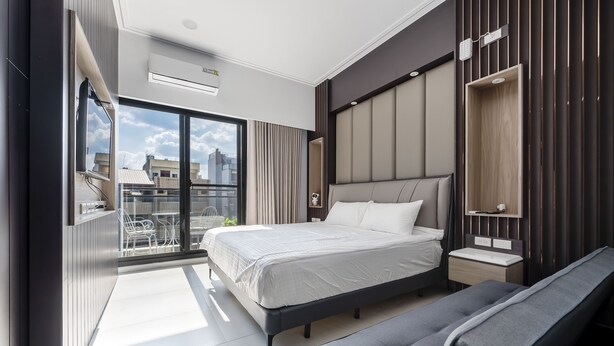 Ein modernes Hotelzimmer mit einem großen Bett, einer Bank, einem kleinen Nachttisch und Blick auf die Stadt durch große Fenster.