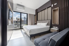 Une chambre d’hôtel moderne avec un grand lit, une banquette, une petite table de chevet et une vue sur la ville grâce à de grandes fenêtres.