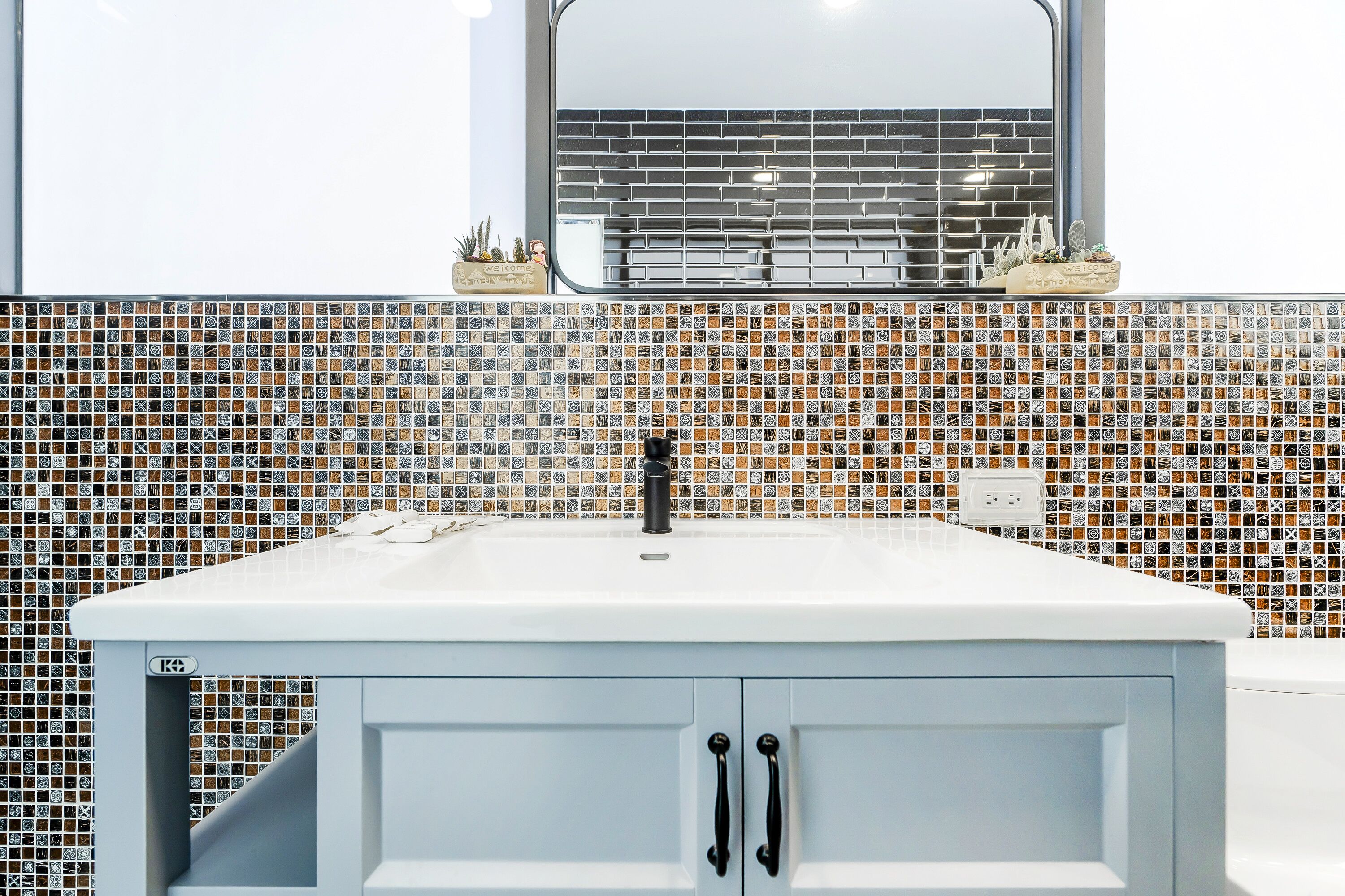 Un baño con lavamanos blanco, grifo negro y un salpicadero de mosaicos.