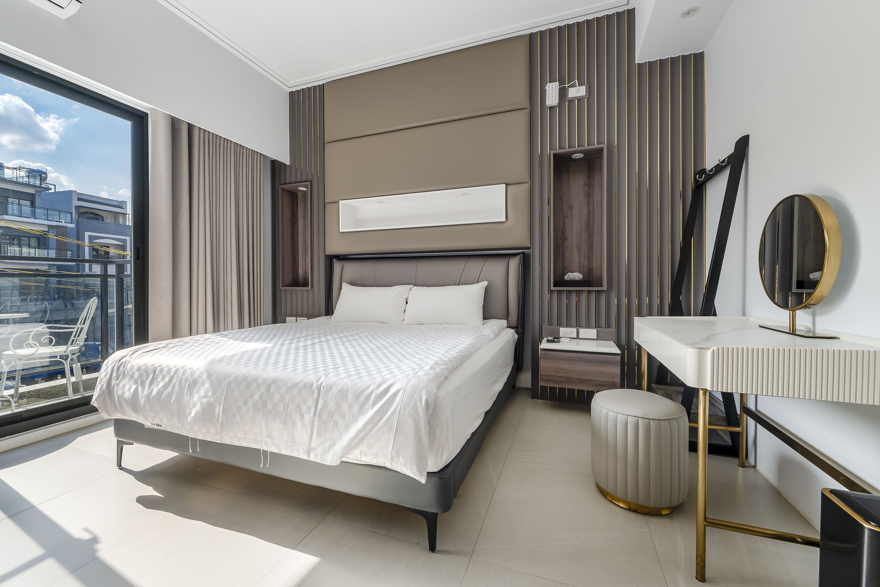A modern bedroom with a large bed, bedside tables, a vanity, and a view of the city.