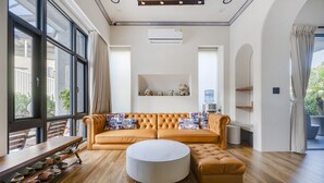 Ein modernes Wohnzimmer mit großem Fenster, einer Sofagarnitur, einem runden Hocker und einem Schuhregal.