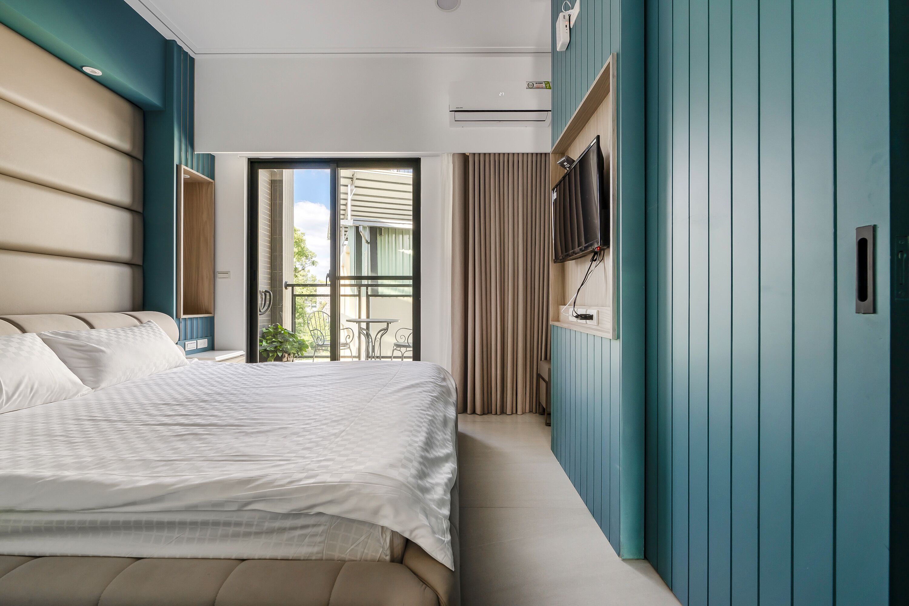 Une chambre d’hôtel moderne dotée d’un grand lit, d’un téléviseur fixé au mur et d’un balcon offrant une vue sur l’extérieur.