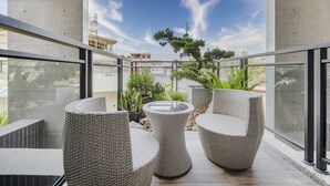 Ein Balkon mit Korbmöbeln, einem Glastisch und Topfpflanzen.