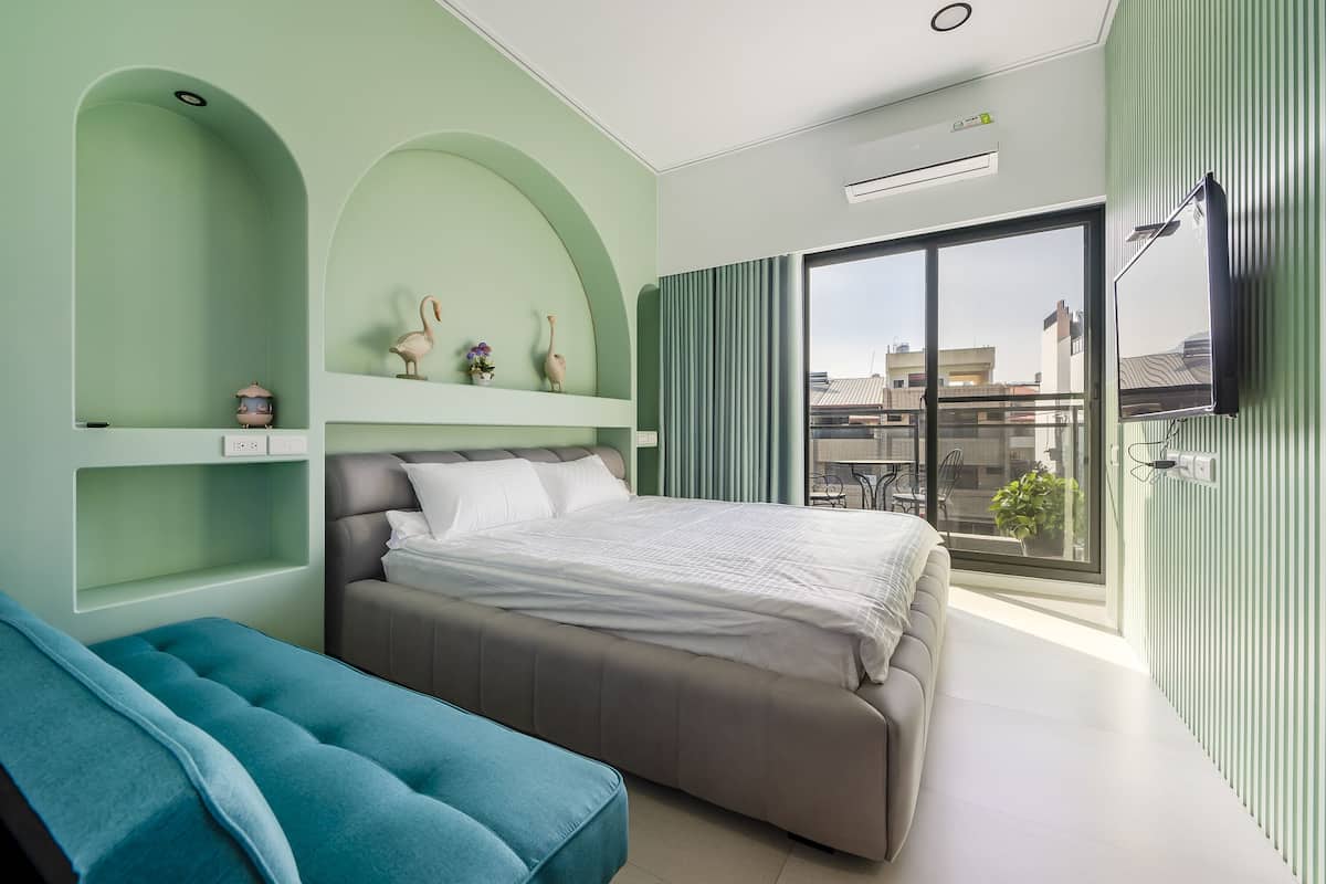 A modern bedroom with a bed, a blue sofa, and a balcony with a view of buildings.
