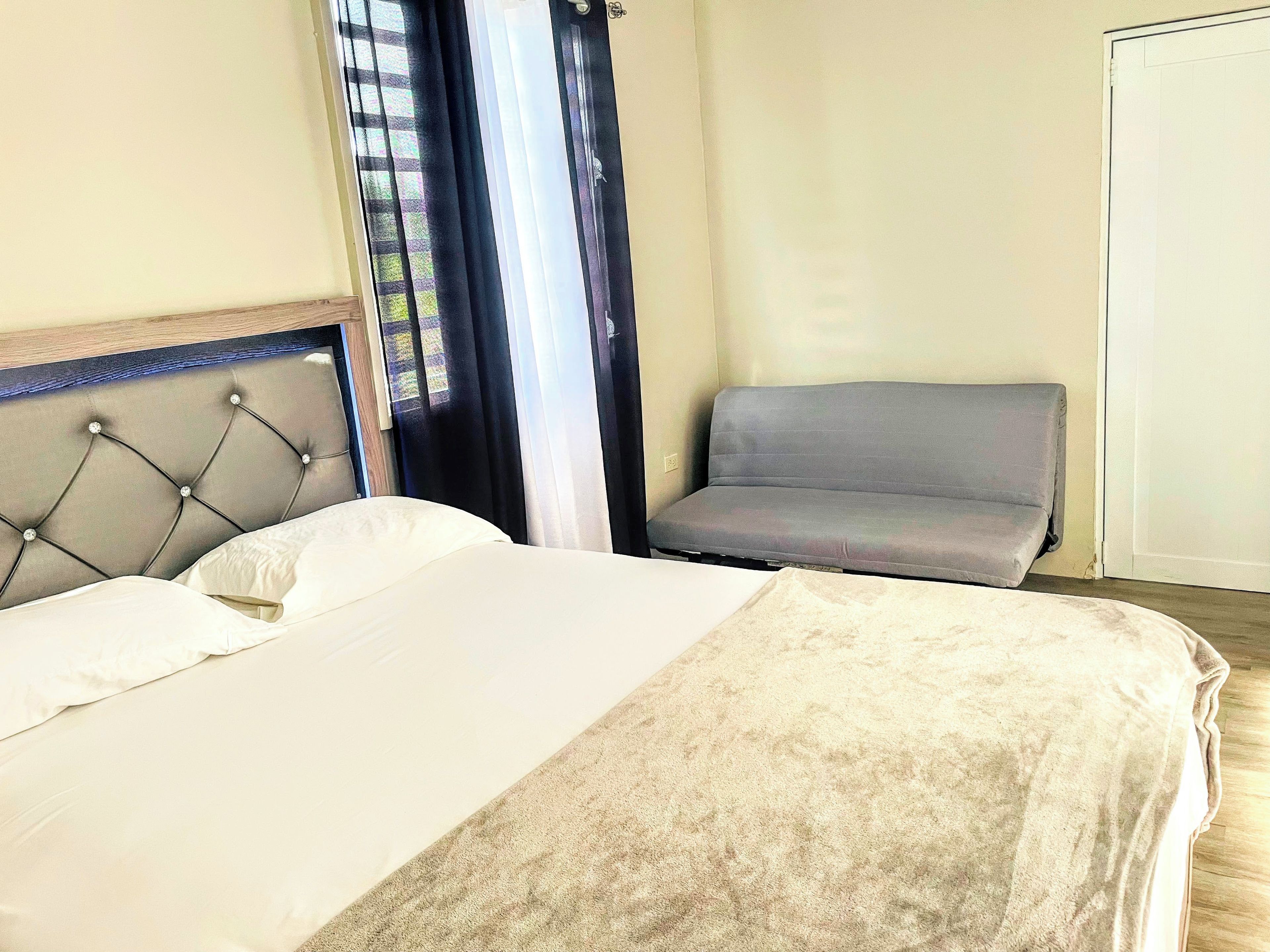 A hotel room with a bed, a grey armchair, and a window with curtains.