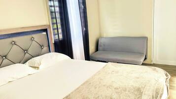 A hotel room with a bed, a grey armchair, and a window with curtains.