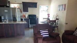 Ein geräumiger Wohnbereich mit braunem Sofa, einem Esstisch und einer Küche im Hintergrund.
