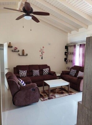 A living room with a brown sofa set, a white coffee table, and a ceiling fan. - Minty Rue Villa

 (Saint Ann's Bay)