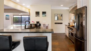 A modern kitchen with a central island, stainless steel appliances, and a view to an outdoor area. - Luxurious Makai Villa with Pool and Ocean Views (Kailua Kona)