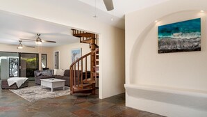 A spacious living area with a wooden staircase, a white coffee table, and a large painting on the wall. - Luxurious Makai Villa with Pool and Ocean Views (Kailua Kona)