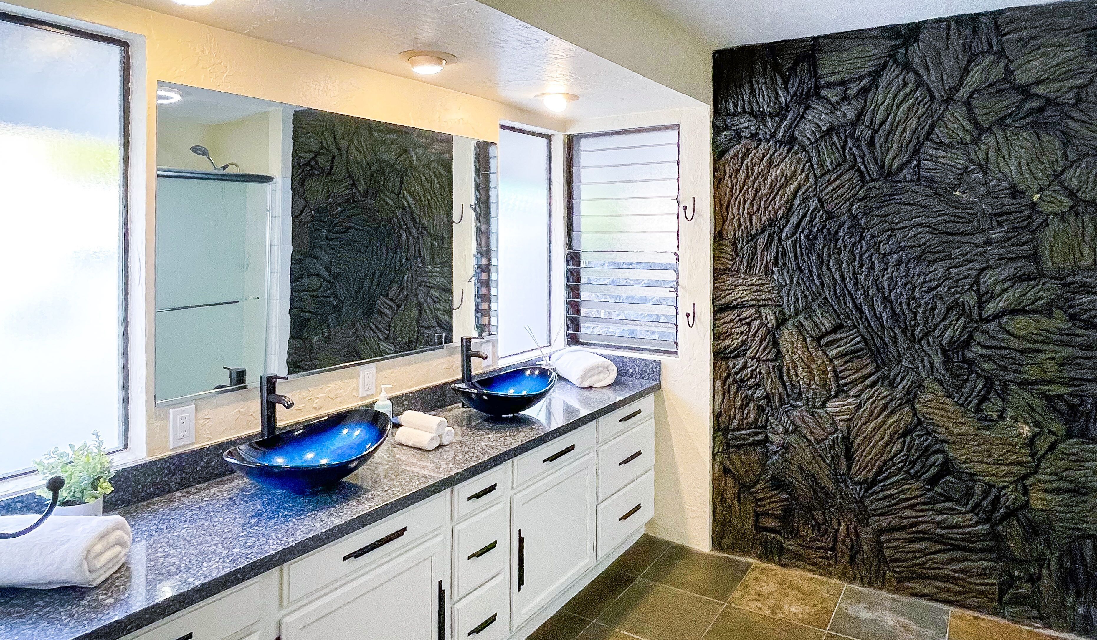A modern bathroom with two sinks, a large mirror, and a textured wall.