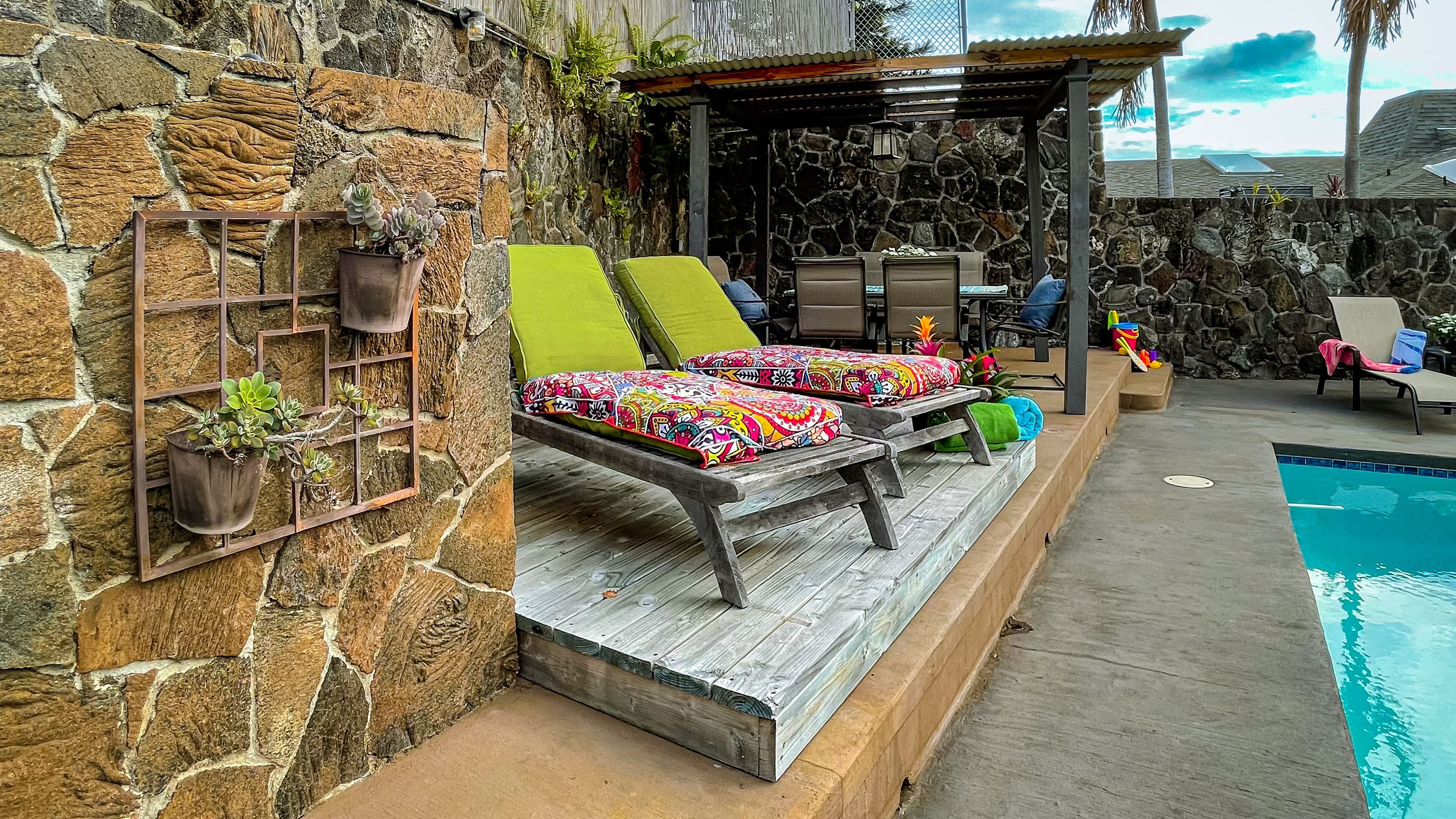 Un mur en pierre agrémenté de jardinières en métal, un espace autour de la piscine avec des chaises longues et un coin salon abrité.
