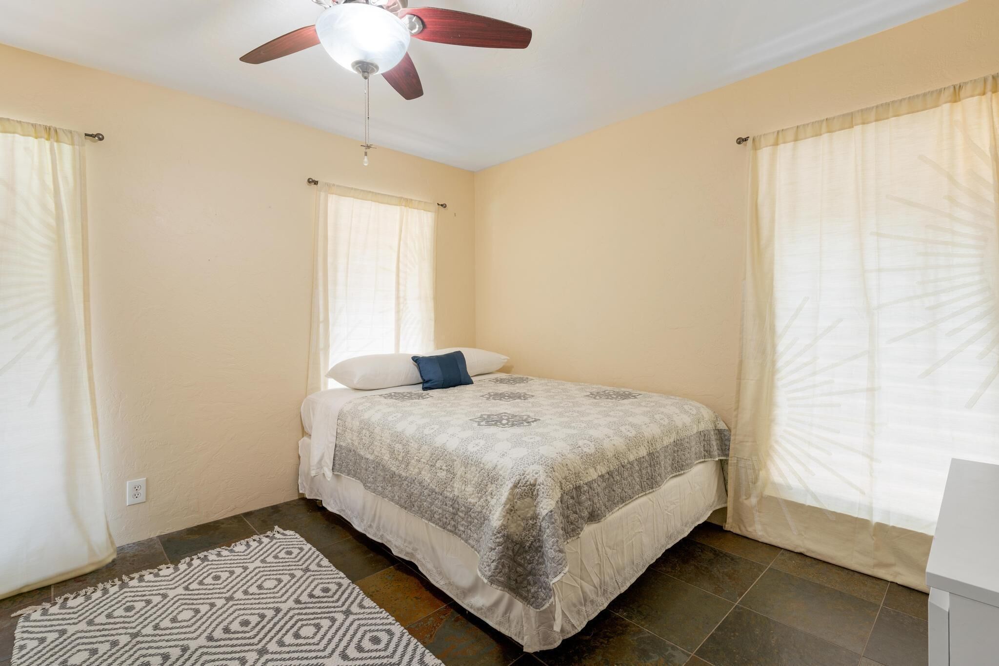 A bedroom with a bed, a ceiling fan, and a window with curtains.