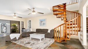 A spacious living room with a wooden spiral staircase, a white coffee table, and a grey sofa. - Luxurious Makai Villa with Pool and Ocean Views (Kailua Kona)
