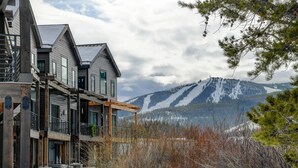A multi-story building with a balcony, a stone wall, and a view of snow-covered mountains.