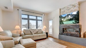 A modern living room with a beige sofa, a fireplace, and a large window with a view of a snowy landscape.