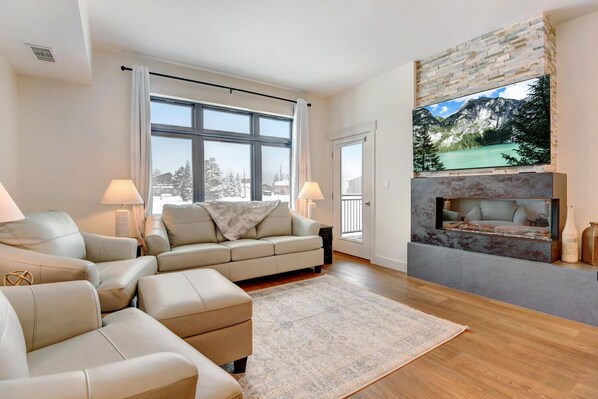 Una sala de estar moderna con un sofá color beige, una chimenea y un ventanal con vistas a un paisaje nevado.