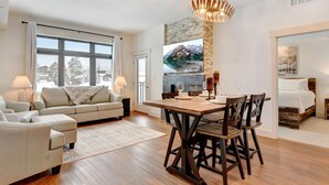 A modern living room with a sofa, a dining table set for four, and a large window with a view of mountains.