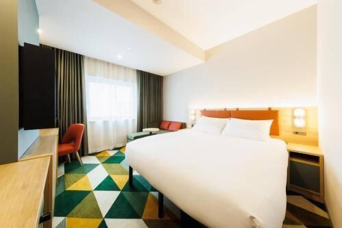 A hotel room with a bed, a desk, a chair, and a window with curtains.