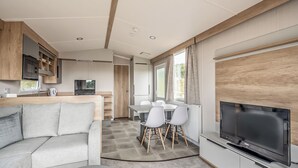 Ein modernes Wohnmobil-Interieur mit Wohnbereich, Küche, Essplatz und einem großen Fernseher.