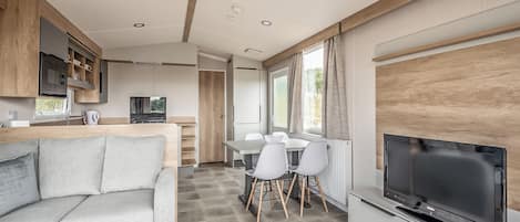 A modern RV interior with a living area, kitchen, dining space, and a large TV.
