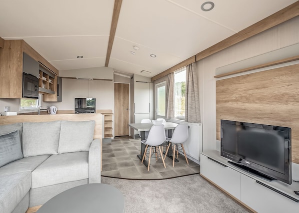 Un intérieur de camping-car moderne comprenant un espace de vie, une cuisine, un coin repas et un grand téléviseur.