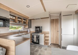 Una cucina compatta con fornelli, forno e lavello, scaffali in legno e una finestra.