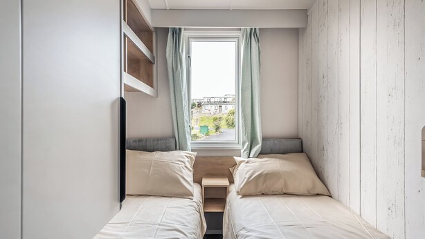 Ein kleines Schlafzimmer mit zwei Betten, einem Fenster mit Vorhängen und Blick ins Freie.