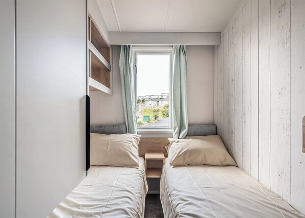 A small bedroom with two beds, a window with curtains, and a view of the outside. - 3 bedroom accommodation in Castle Douglas (Castle Douglas)