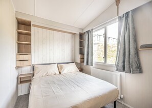 Camera da letto con un letto, mensole a muro, una finestra con tende e un termosifone.