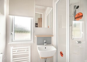 Un bagno con finestra, lavandino, specchio e box doccia in vetro.