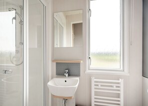 A bathroom with a glass shower enclosure, a white sink, a mirror, and a window with a view.