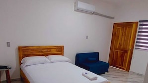 Une chambre avec un lit en bois, une chaise bleue et un appareil de climatisation fixé au mur.