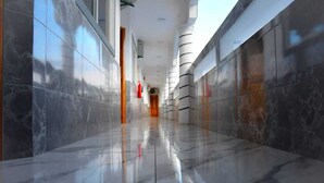 Un couloir aux murs et au sol recouverts de marbre poli, qui mène à une porte sur laquelle est fixé un extincteur.