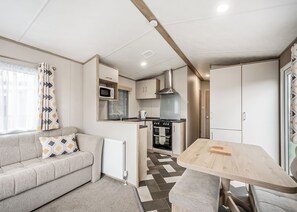 A compact kitchenette with a microwave, oven, and stove, a sofa with patterned cushions, and a dining table with a bench.