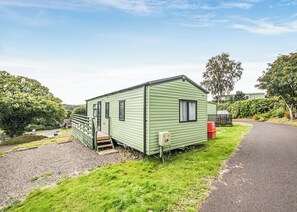 A green mobile home with a porch and steps, located next to a paved path.