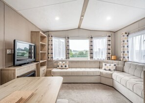 A modern living room with a sofa, TV, wooden table, and a view of the outdoors.