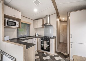 A compact kitchen with a microwave, stove, oven, and a window with blinds.