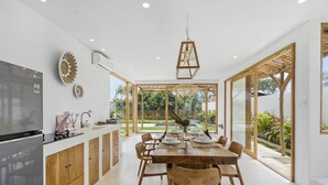 Eine moderne Küche mit Essbereich, Holzschränken, einem großen Kühlschrank und Blick in den Garten durch Glastüren.