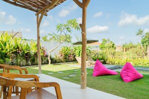 A patio with wooden furniture, a grassy area, and a bamboo fence.
