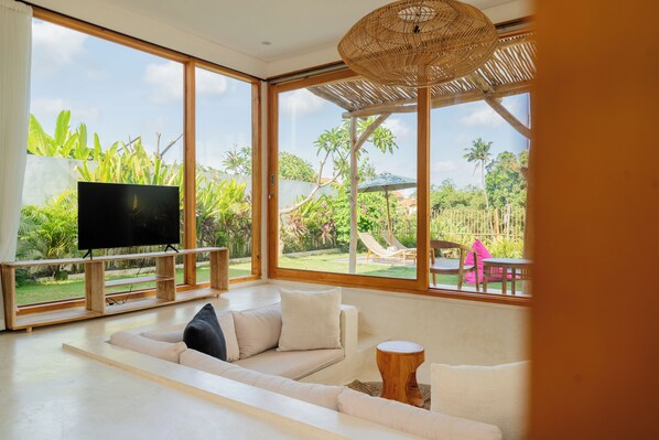 Un salon moderne doté d’un grand téléviseur, de sièges confortables et offrant une vue sur un jardin luxuriant.