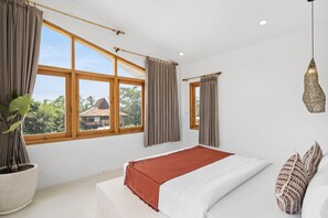 A bedroom with a large bed, two windows with curtains, a hanging light fixture, and a potted plant.