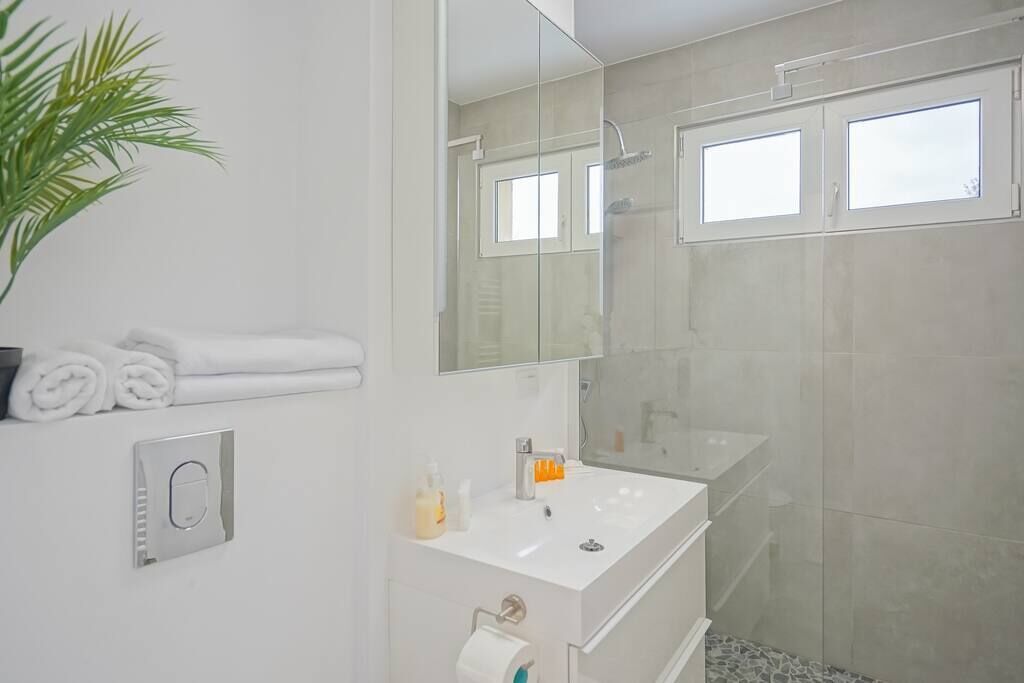 Een moderne badkamer met een grote spiegel, een wit wastafelmeubel en een douchehoek.
