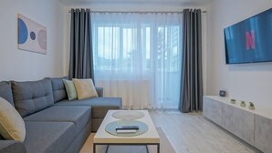 A modern living room with a grey sofa, a coffee table with a remote control, a TV on the wall, and a large window with grey curtains. - Mountain Hideaway w. Netflix and Mountain View (Brașov)